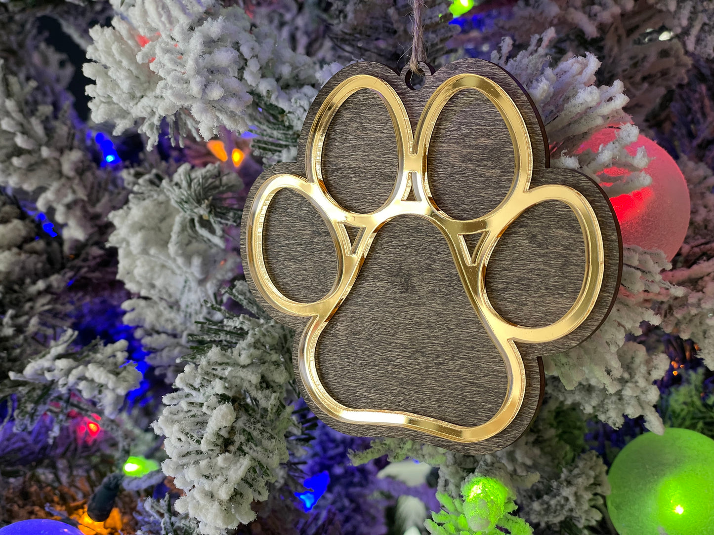 Dog Paw ornament hanging on Christmas Tree. The ornament is wooden, the dog paw is mirror gold.